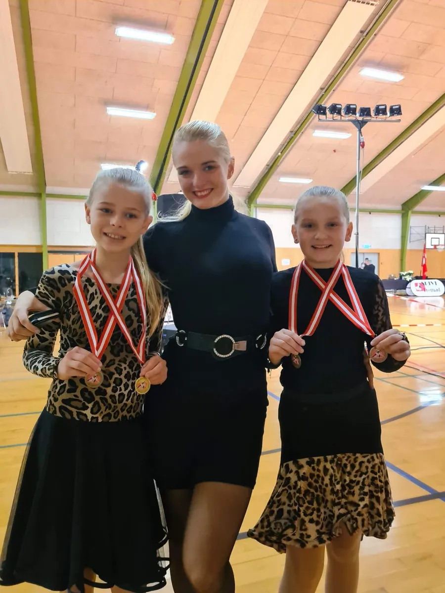 To dansere med medaljer sammen med instruktøren